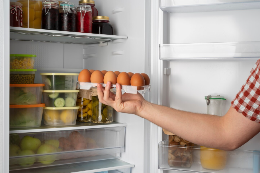Organized fridge with clear bins and a person storing eggs on a middle shelf, demonstrating refrigerator zones.